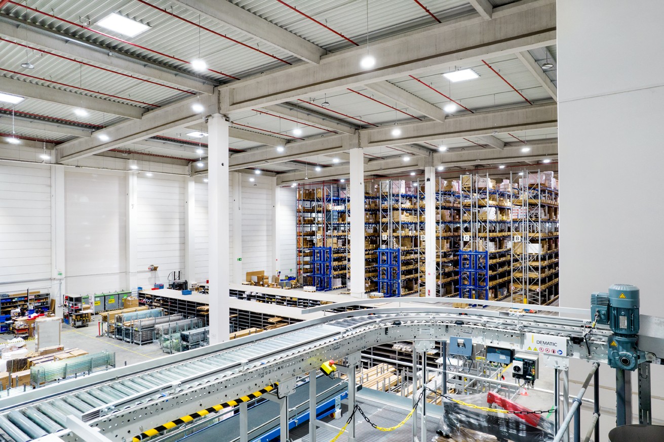 Imagen corporativa de RS de un almacén de estanterías altas desde la perspectiva interior, mostrando los diferentes niveles y una línea de montaje.