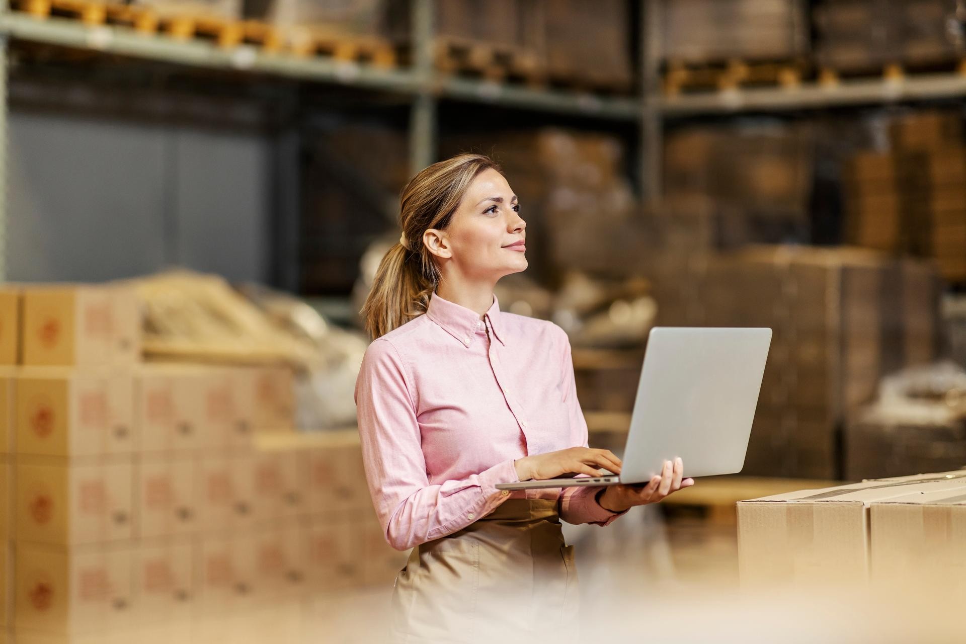 Procurement professional in a warehouse ordering new supplies with a laptop