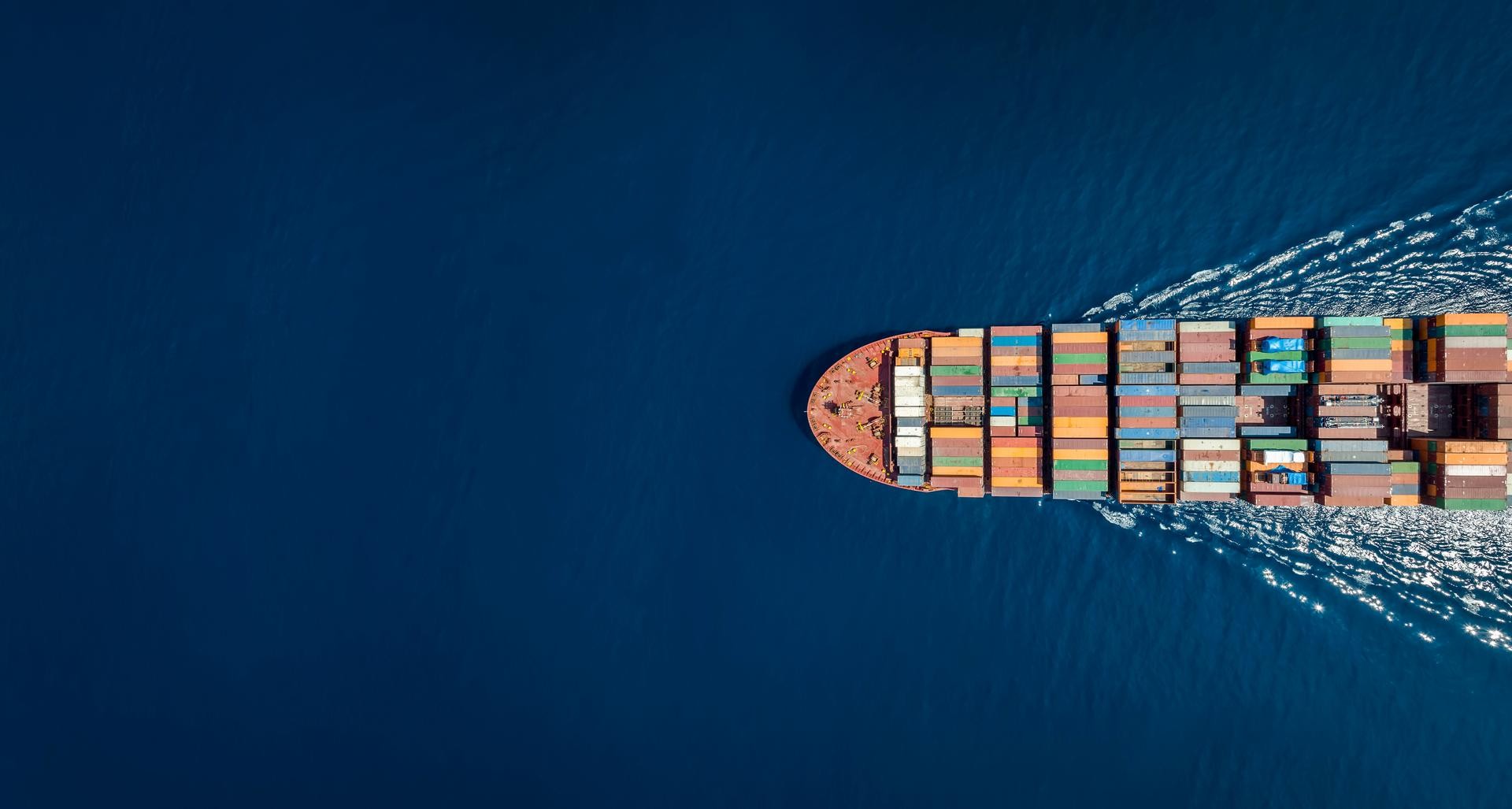 Schip met containers vanuit vogelperspectief vaart naar links in de open zee 