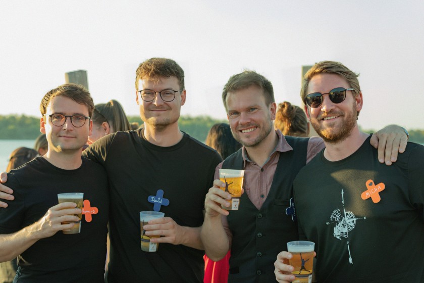 Vier jonge mannen met zwarte kleding lachen naar de camera met bier in hun hand