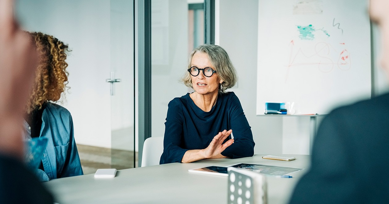 Vrouw op kantoor aan een tafel legt iets uit aan collega